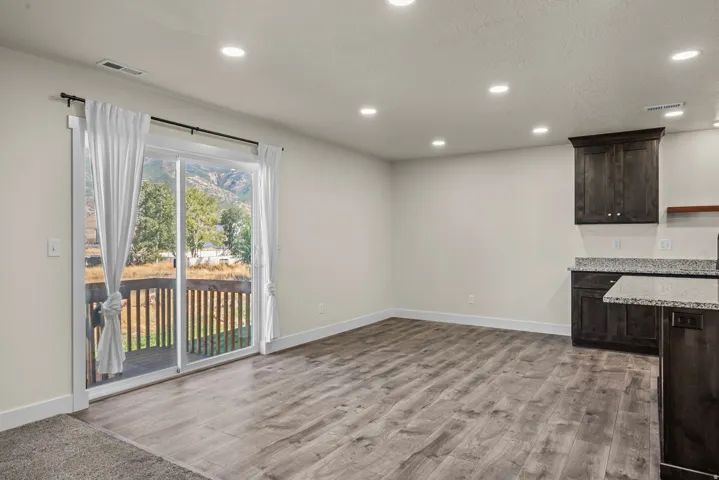 Wood-finish flooring, recessed lighting, sliding glass door, private deck, and dark wood cabinetry with granite countertops