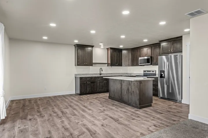 Kitchen featuring dark wood cabinetry, a central island with a solid surface countertop, stainless steel appliances, and recessed lighting
