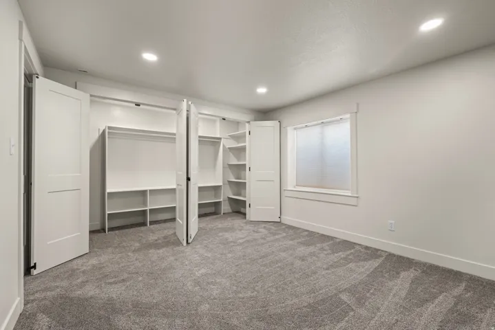 Plush carpeted flooring, recessed ceiling lighting, a window with trim, and built-in closet shelving