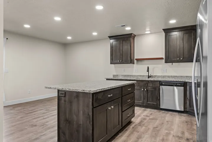 Kitchen featuring wood-finish flooring, recessed lighting, dark wood cabinetry, light-toned countertops, and a kitchen island with integrated power outlets