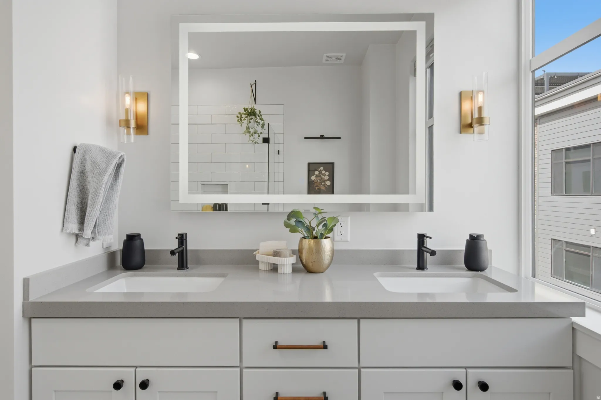 Dual undermount sinks with matte black fixtures, integrated countertop, and an illuminated mirror