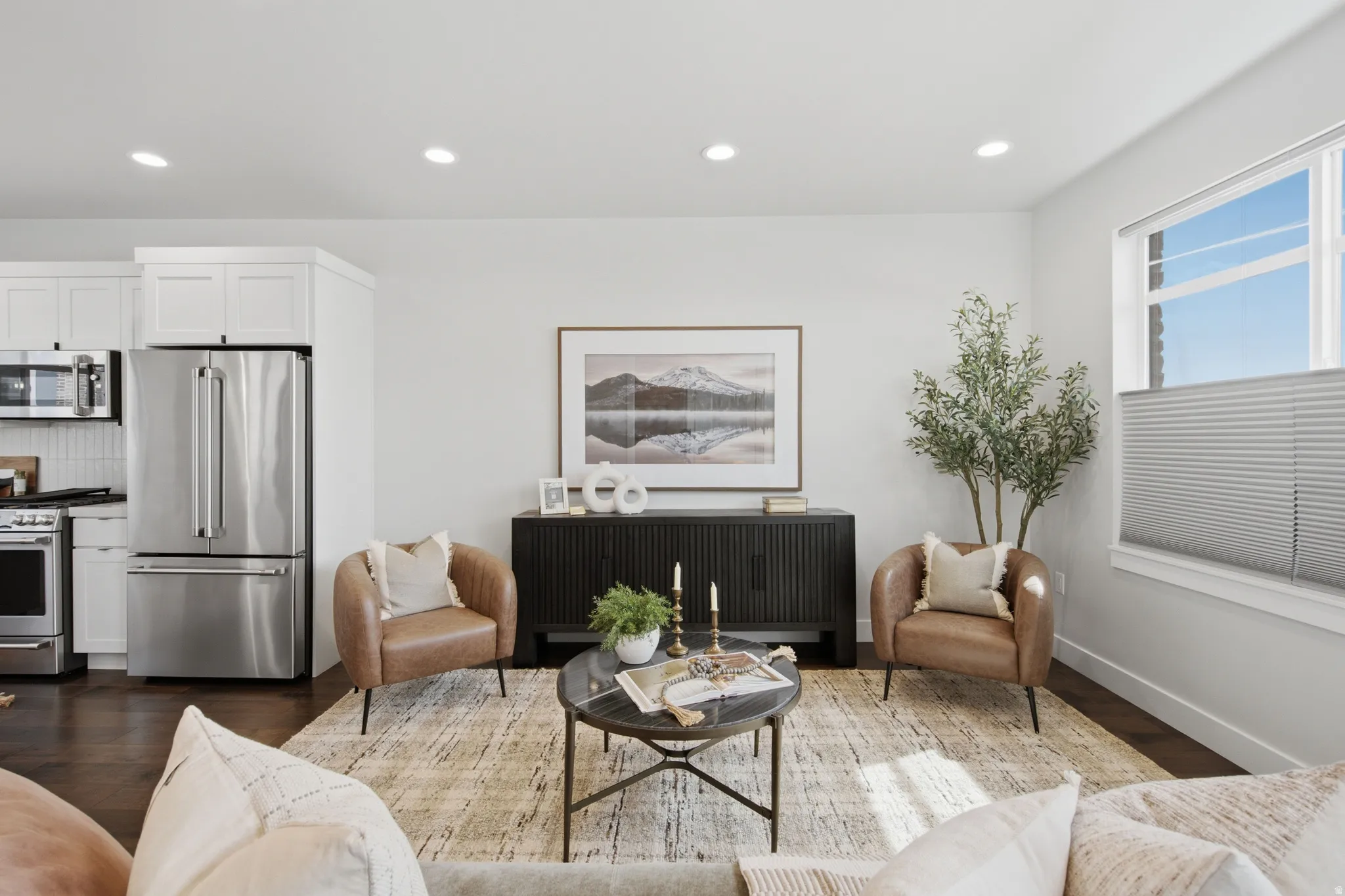 Recessed lighting, wood-finish flooring, white cabinetry, stainless steel appliances, and a large window with privacy blinds
