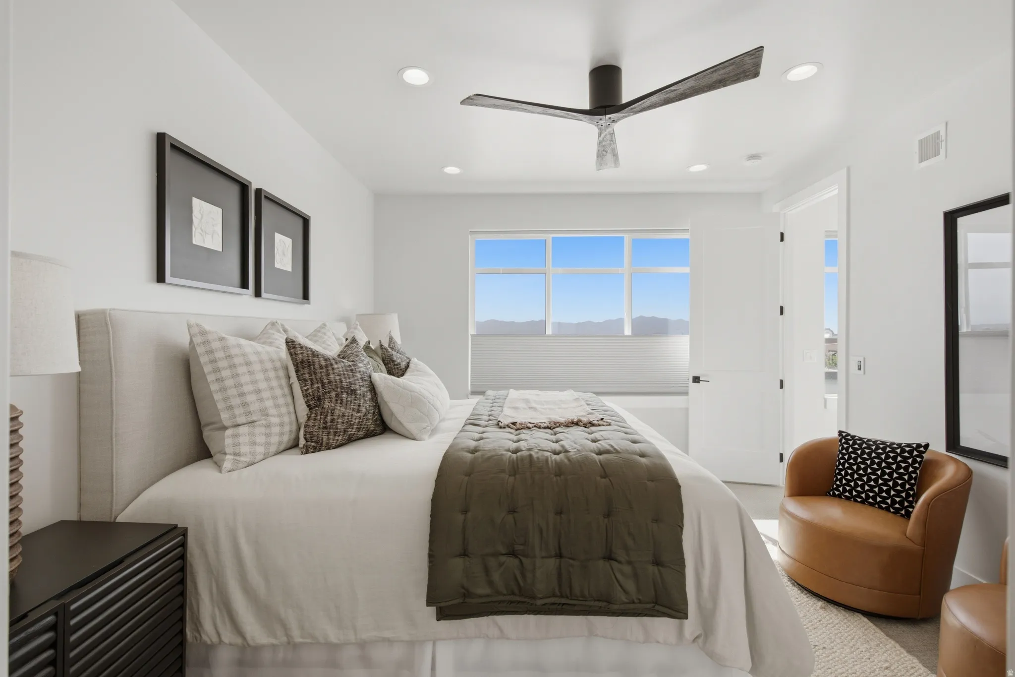 Recessed ceiling lighting, wide horizontal window, modern ceiling fan, white paneled door, and a built-in upholstered headboard