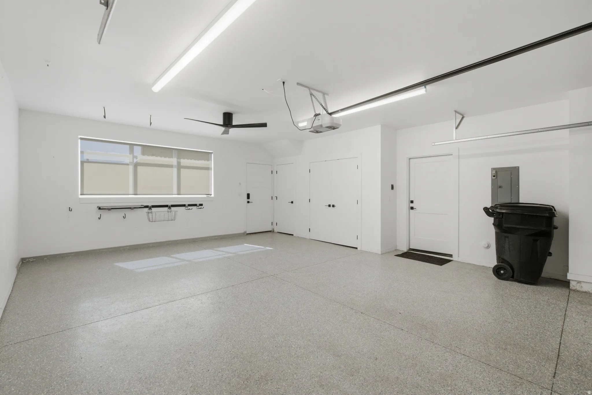 Spacious garage featuring a durable epoxy floor, multiple white panel doors, a large window with roller shades, and integrated overhead lighting