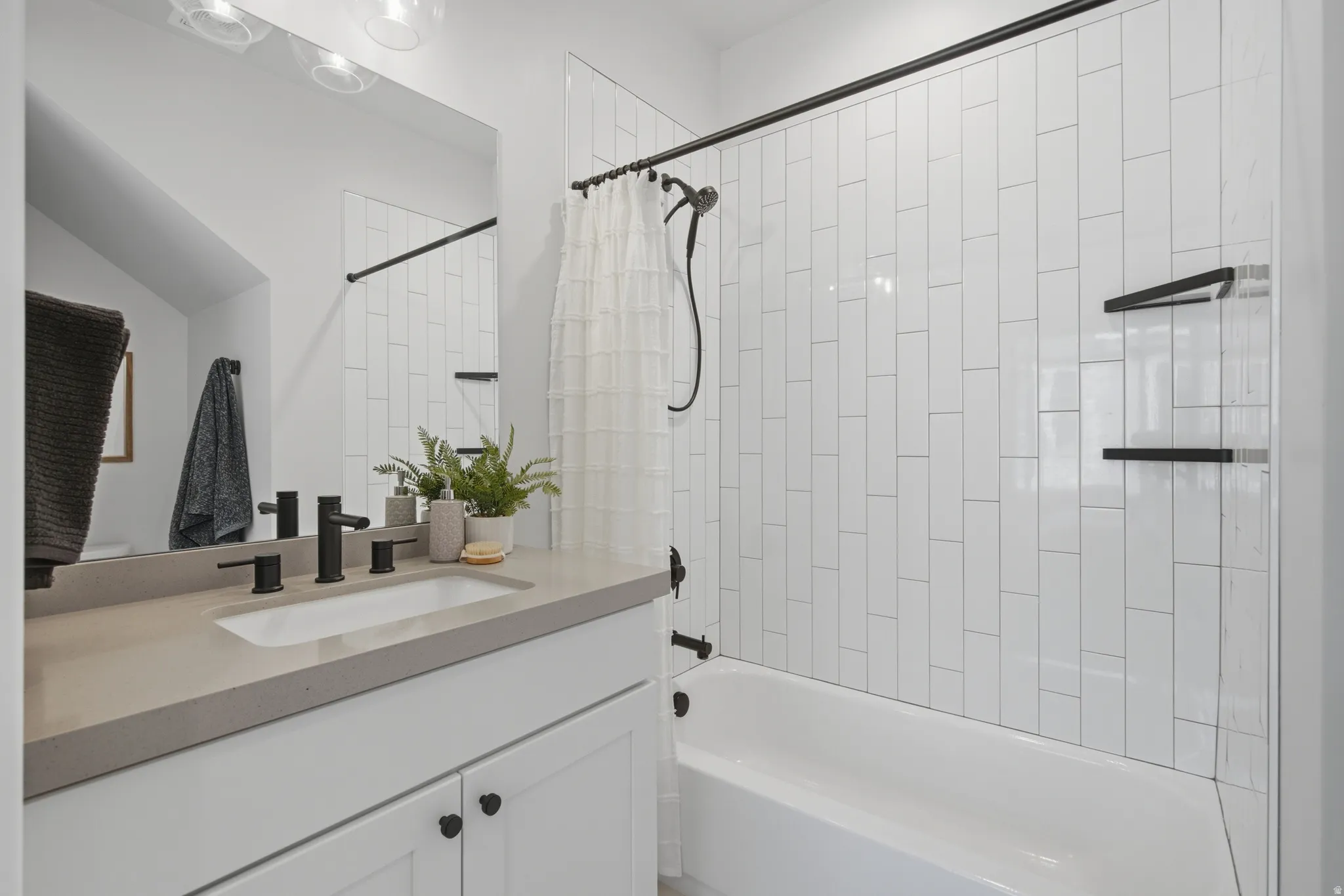 White subway tile shower surround with integrated shelves, matte black fixtures, white vanity with stone countertop, and an undermount sink