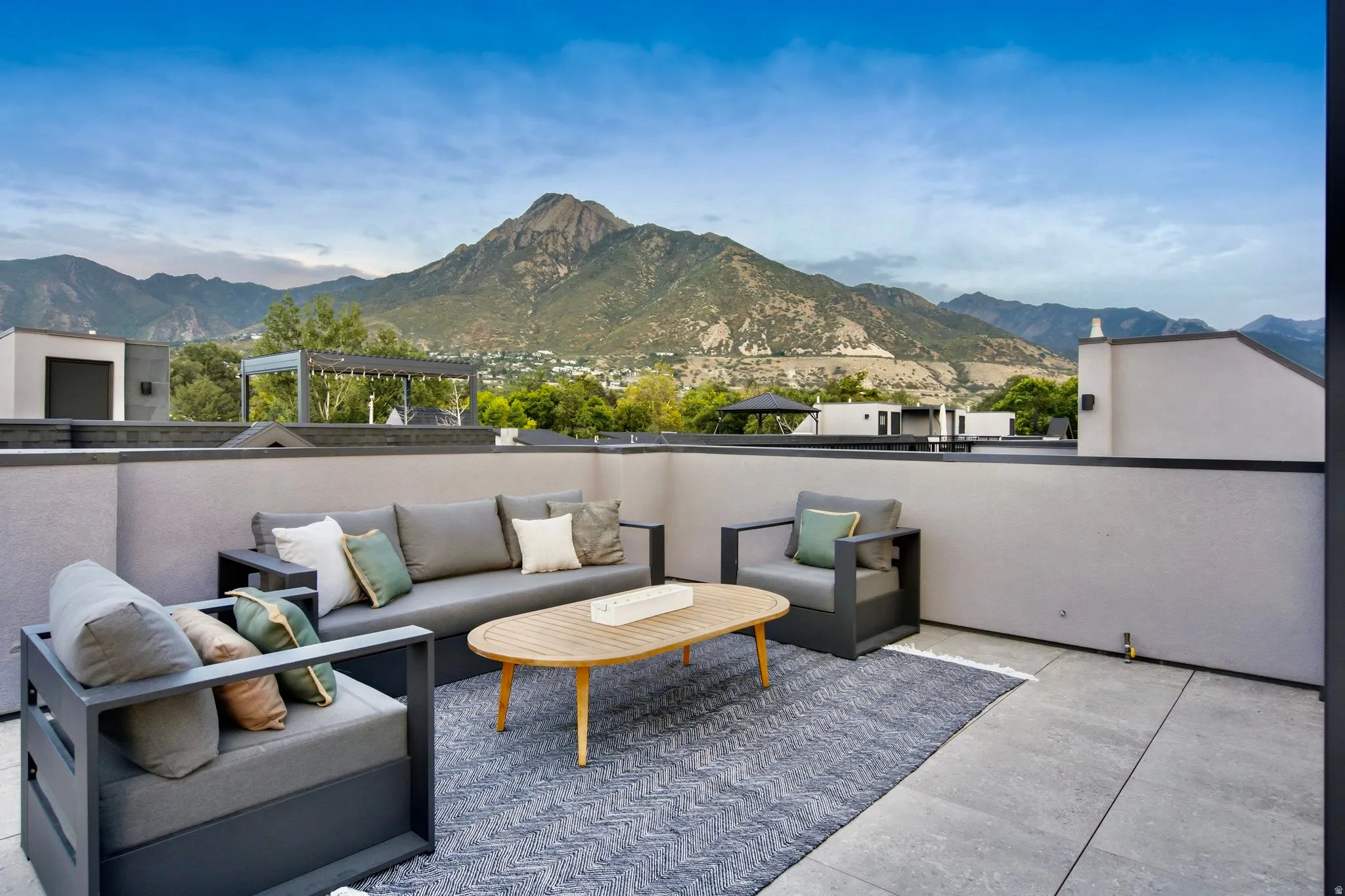 Expansive rooftop patio with mountain backdrop, concrete paver flooring, and perimeter wall