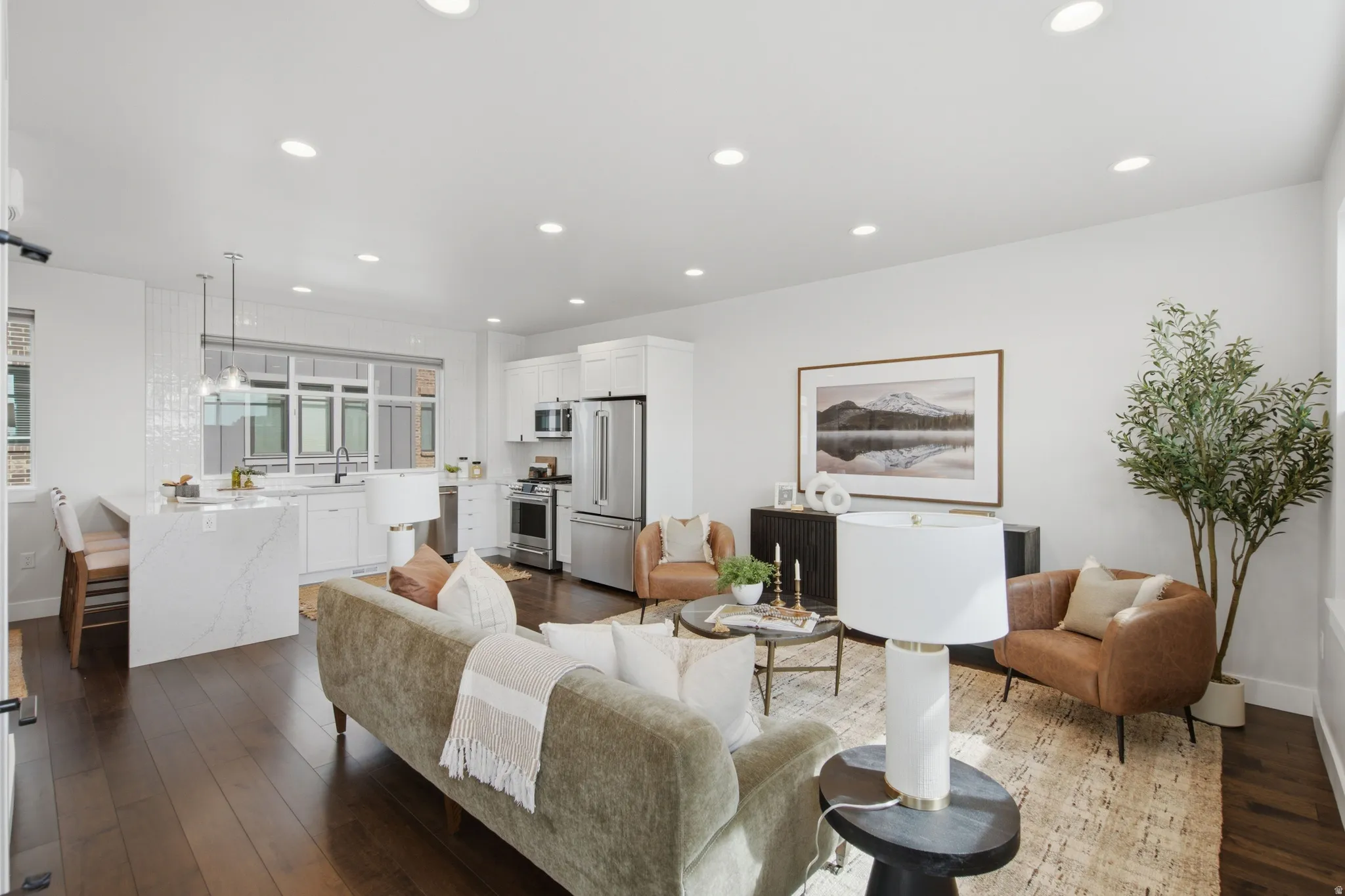 Open concept living space featuring wood-finish flooring, recessed lighting, and a white kitchen with stainless steel appliances and a waterfall island