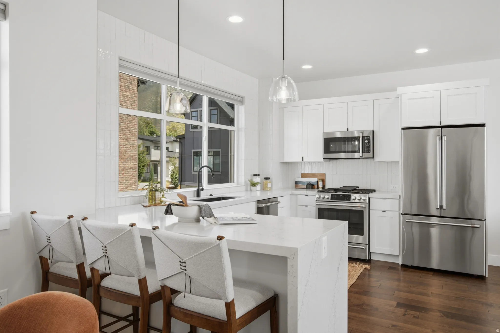 Modern kitchen featuring white shaker cabinetry, stainless steel appliances, a large center island with a waterfall countertop, and wood-finish flooring