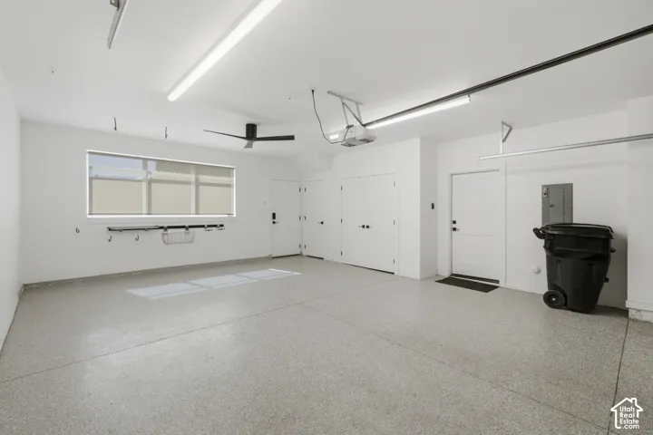Spacious garage featuring a durable epoxy floor, multiple white panel doors, a large window with roller shades, and integrated overhead lighting