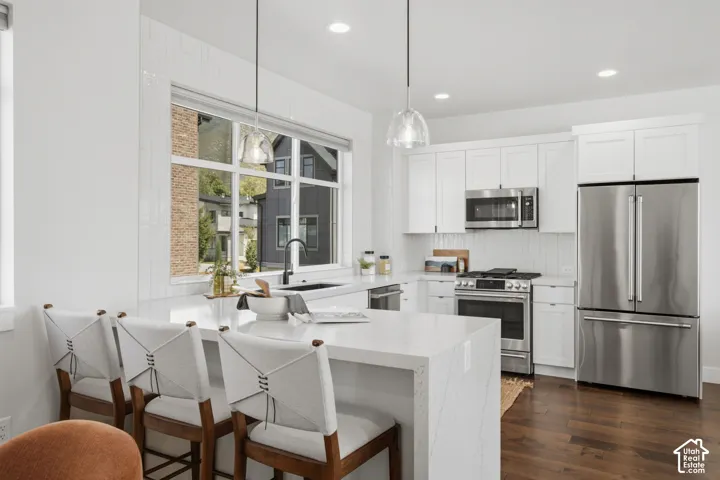 Modern kitchen featuring white shaker cabinetry, stainless steel appliances, a large center island with a waterfall countertop, and wood-finish flooring