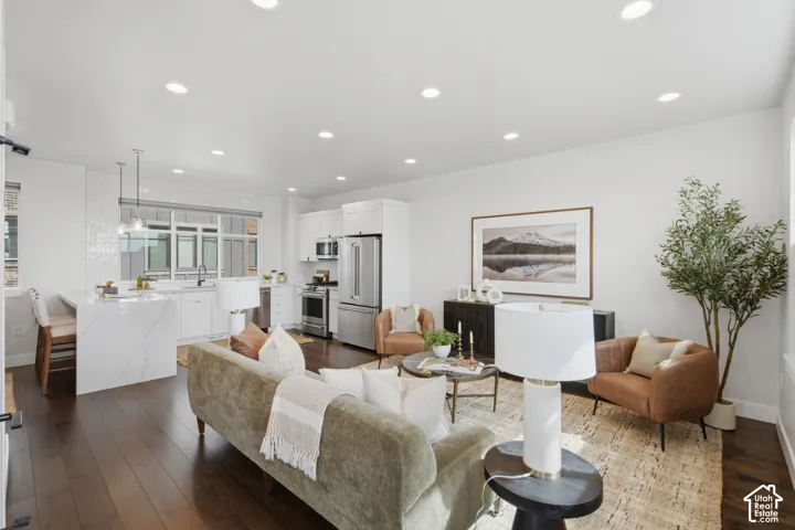 Open concept living space featuring wood-finish flooring, recessed lighting, and a white kitchen with stainless steel appliances and a waterfall island