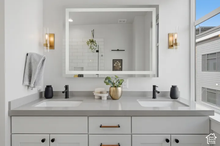 Dual undermount sinks with matte black fixtures, integrated countertop, and an illuminated mirror