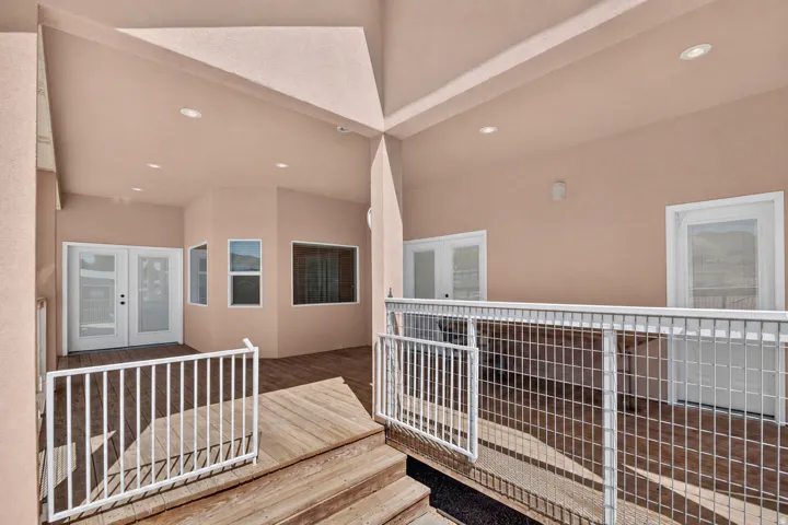 Expansive wood deck with white railing, recessed lighting, and multiple windows