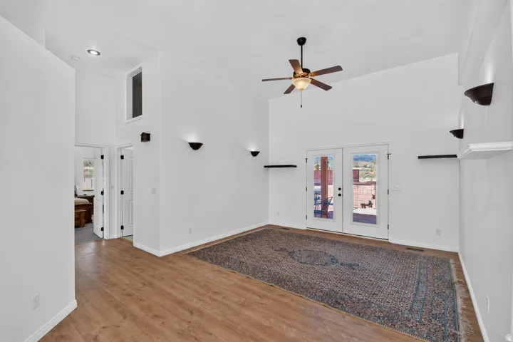 Vaulted ceilings with recessed lighting, wood-finish flooring, ceiling fan, double glass-paneled doors, and wall-mounted sconces