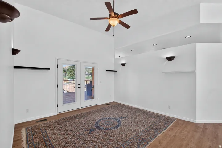 Vaulted ceilings, a ceiling fan, recessed lighting, and wall sconces illuminate this space, featuring wood-finish flooring and double glass doors