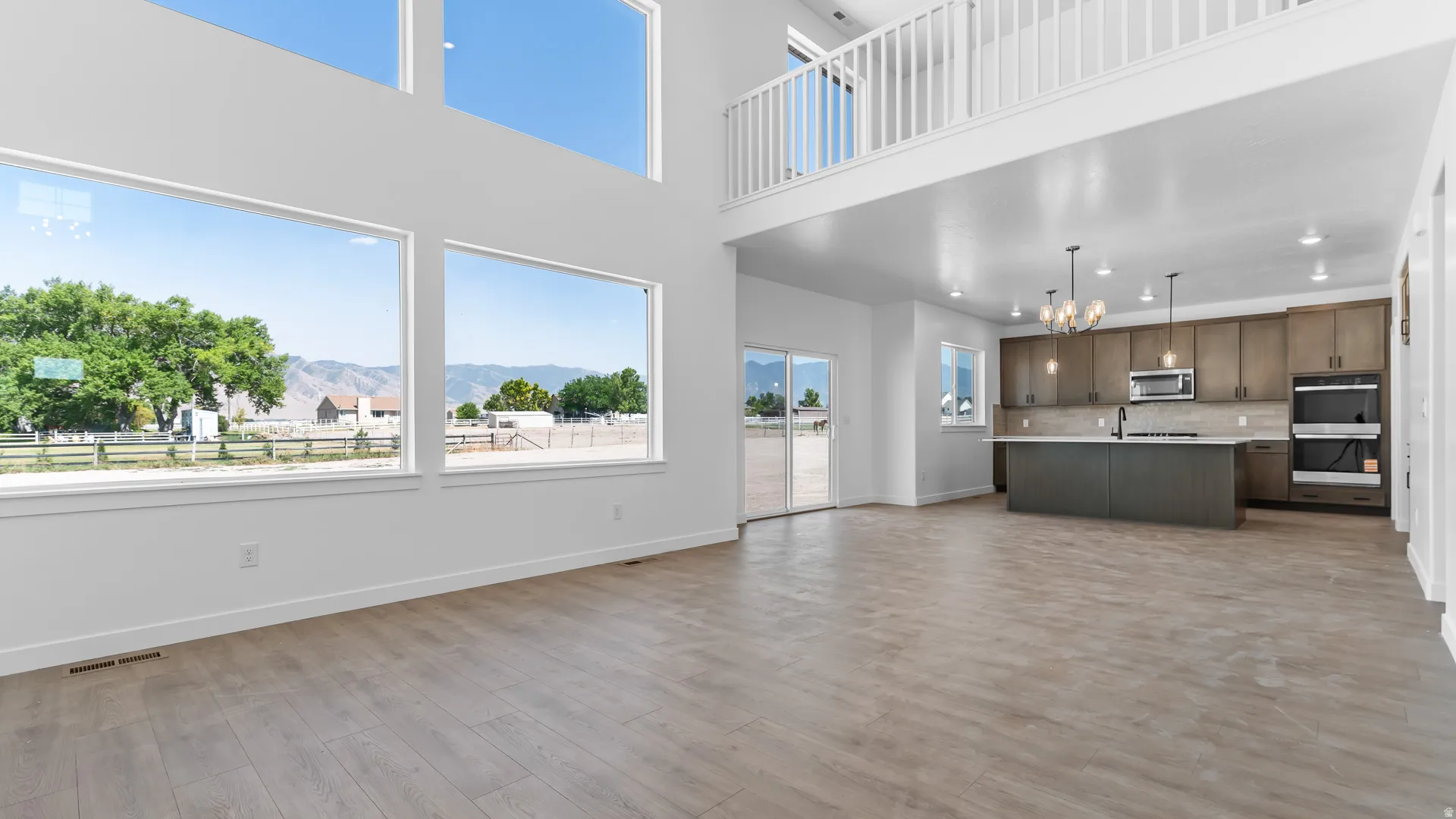 Two-story ceiling with a balcony, large windows, wood-finish flooring, sliding glass doors, and a kitchen with an island