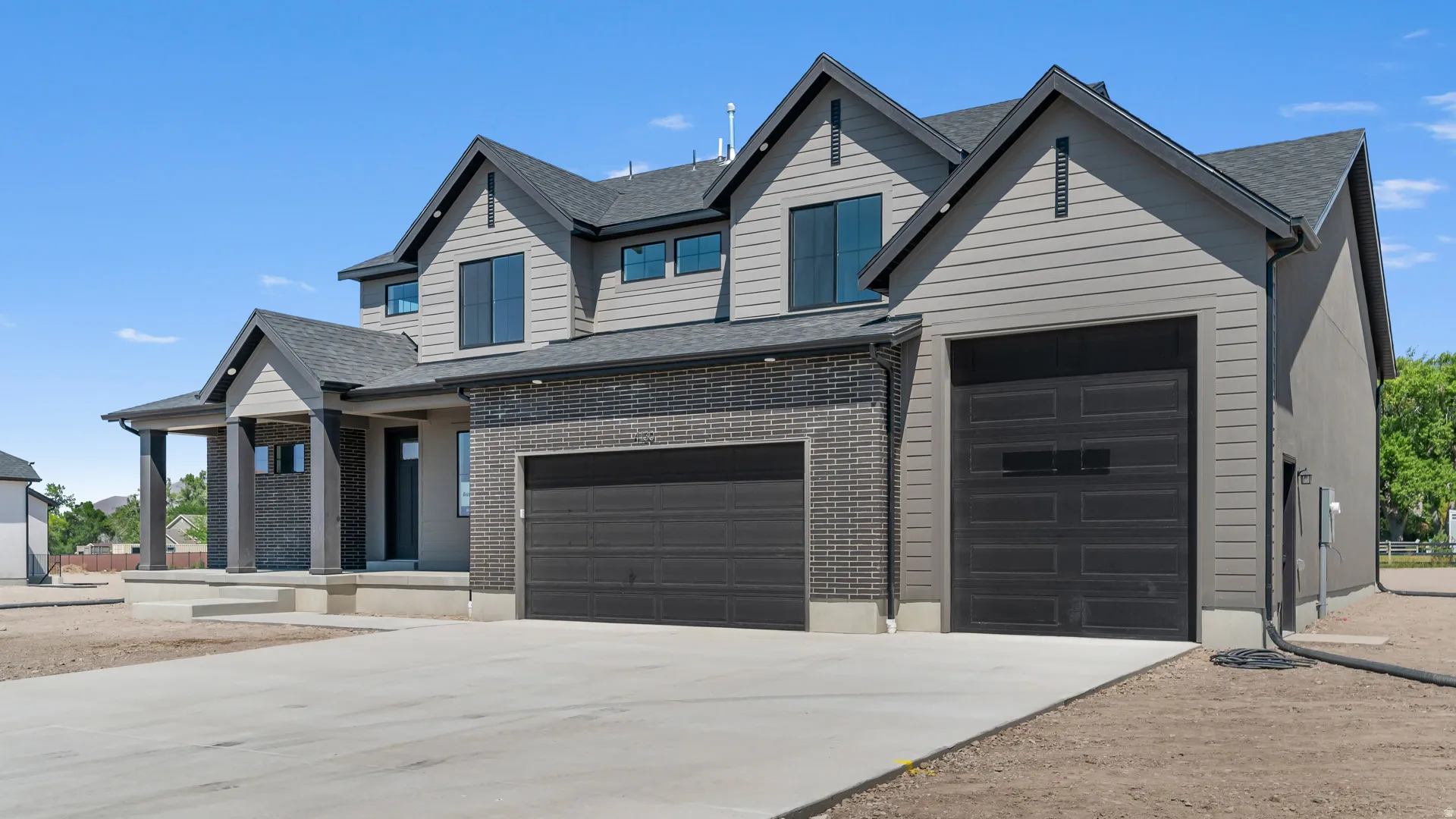 Modern exterior featuring black brick accents, gray siding, a multiple-car garage, and a covered entry