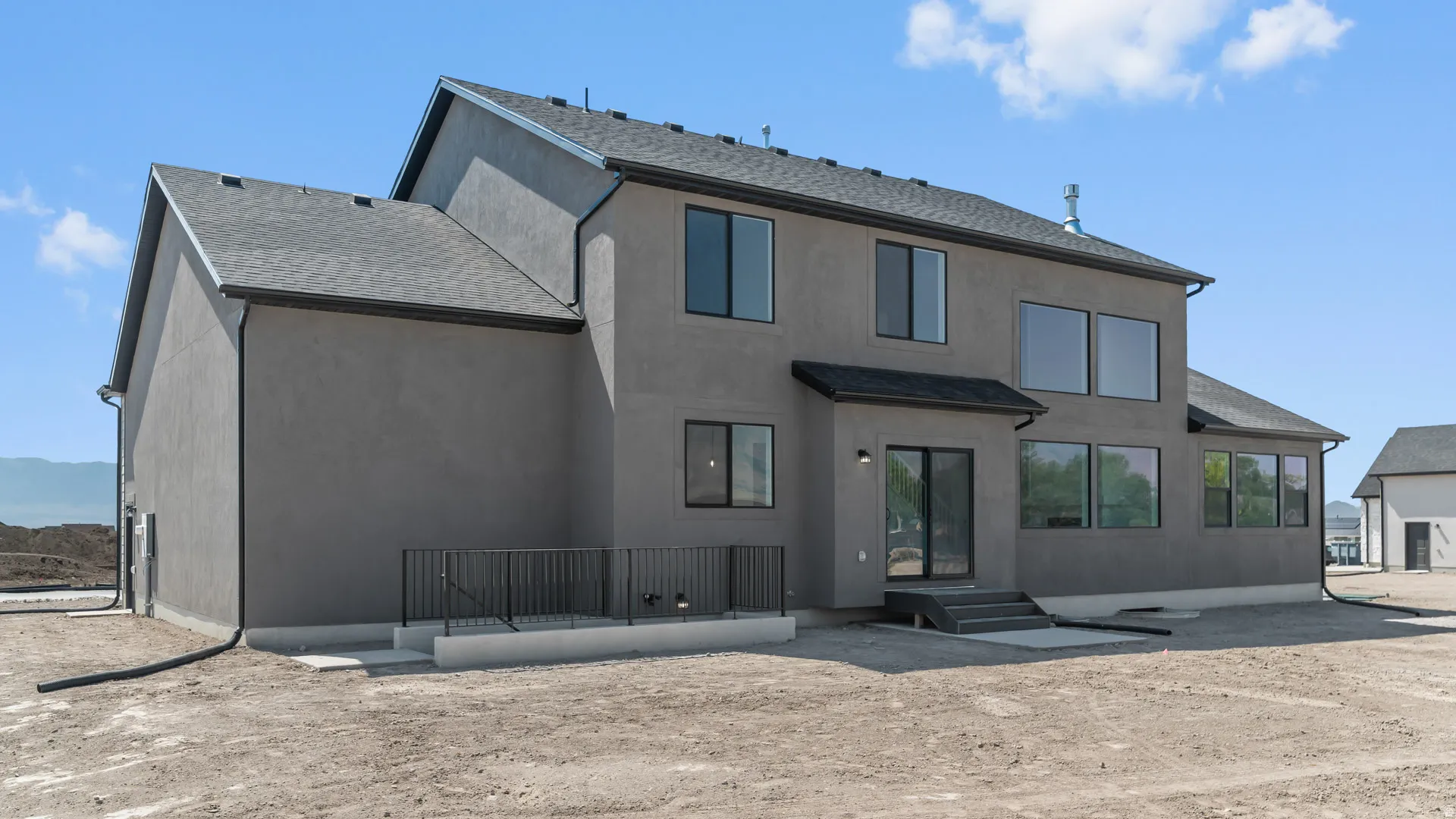 Contemporary stucco exterior with a dark shingle roof, multiple windows, a rear patio with railings, and a sliding glass door
