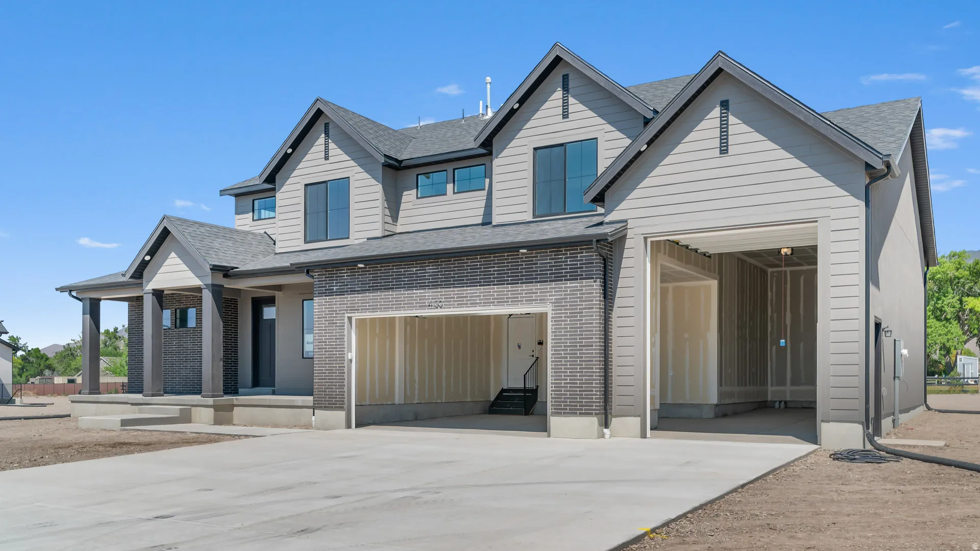 Two-story residence featuring a dark brick facade, light gray siding, and a covered porch with dark wood-wrapped columns