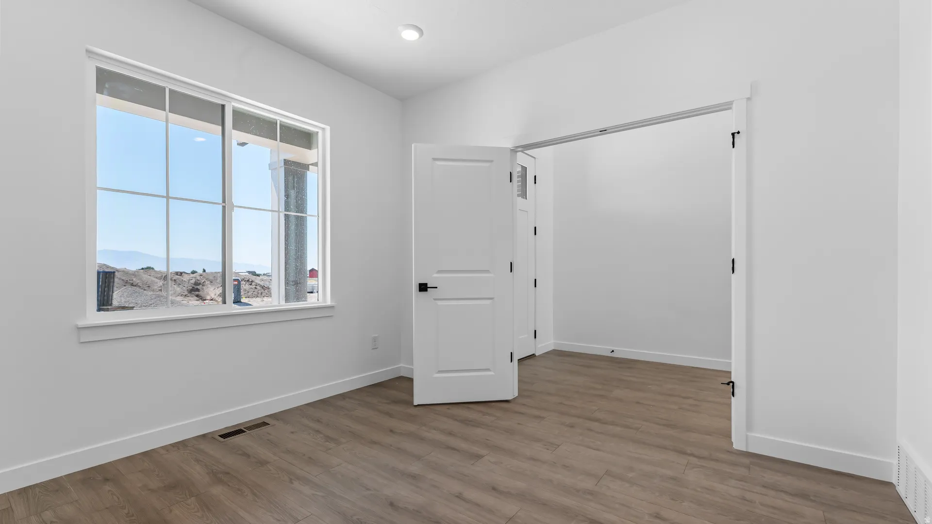 Recessed lighting, wood-finish flooring, white trim, white paneled doors with matte black hardware, and a window with white sashes