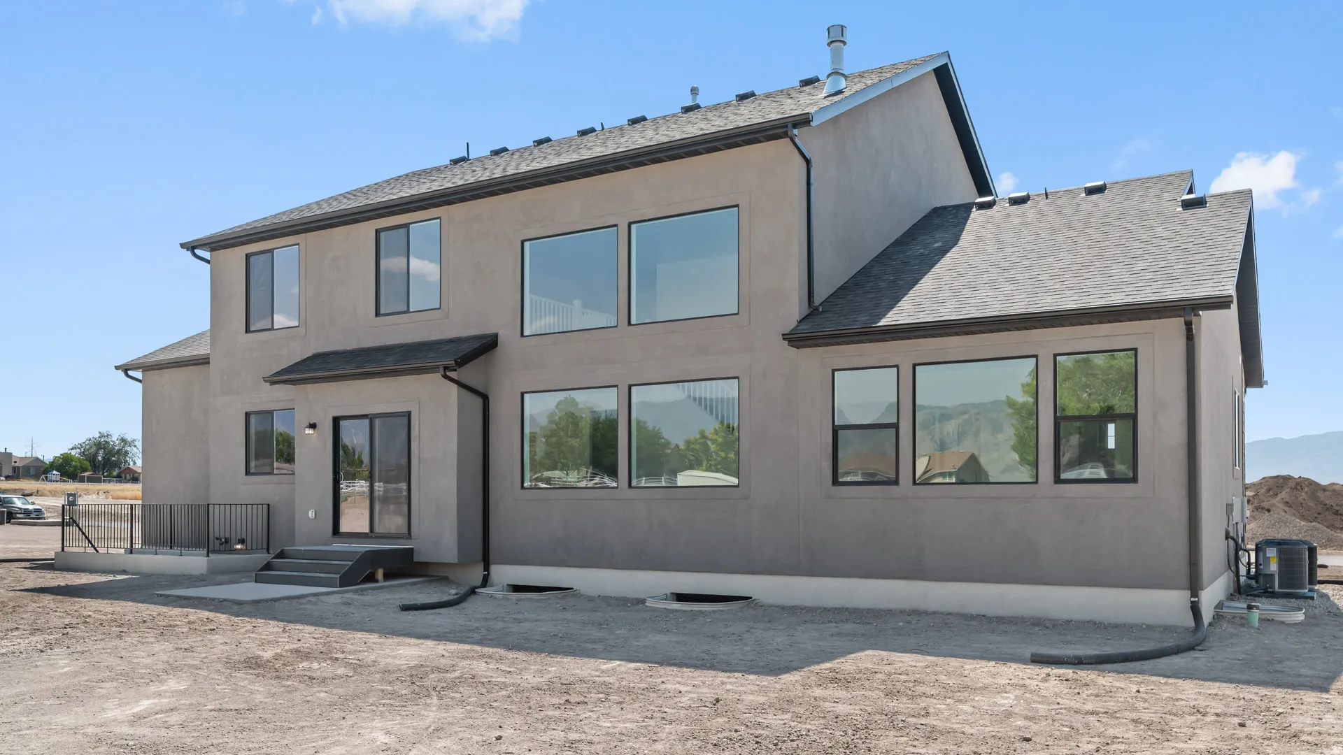 Stucco exterior with multiple large windows, a ground-level patio, and sliding glass doors