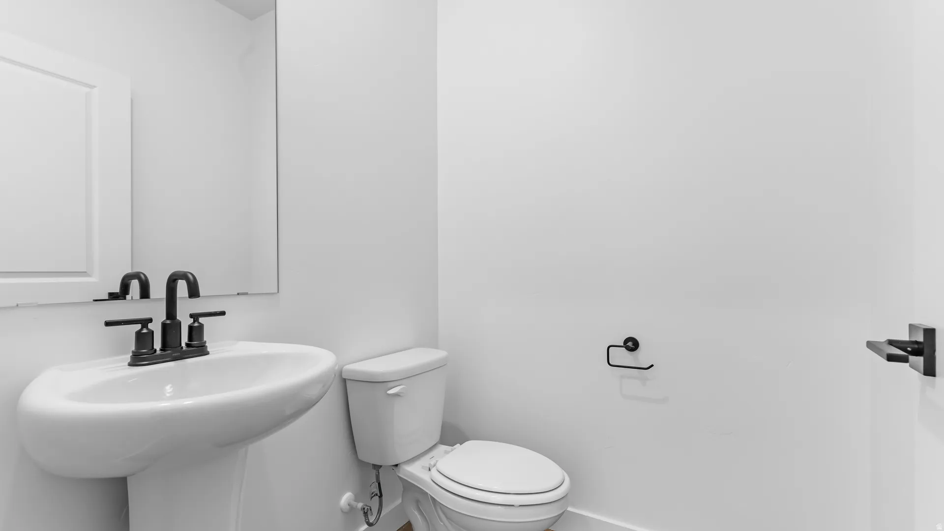 Pedestal sink with a matte black faucet, rectangular wall mirror, and modern toilet