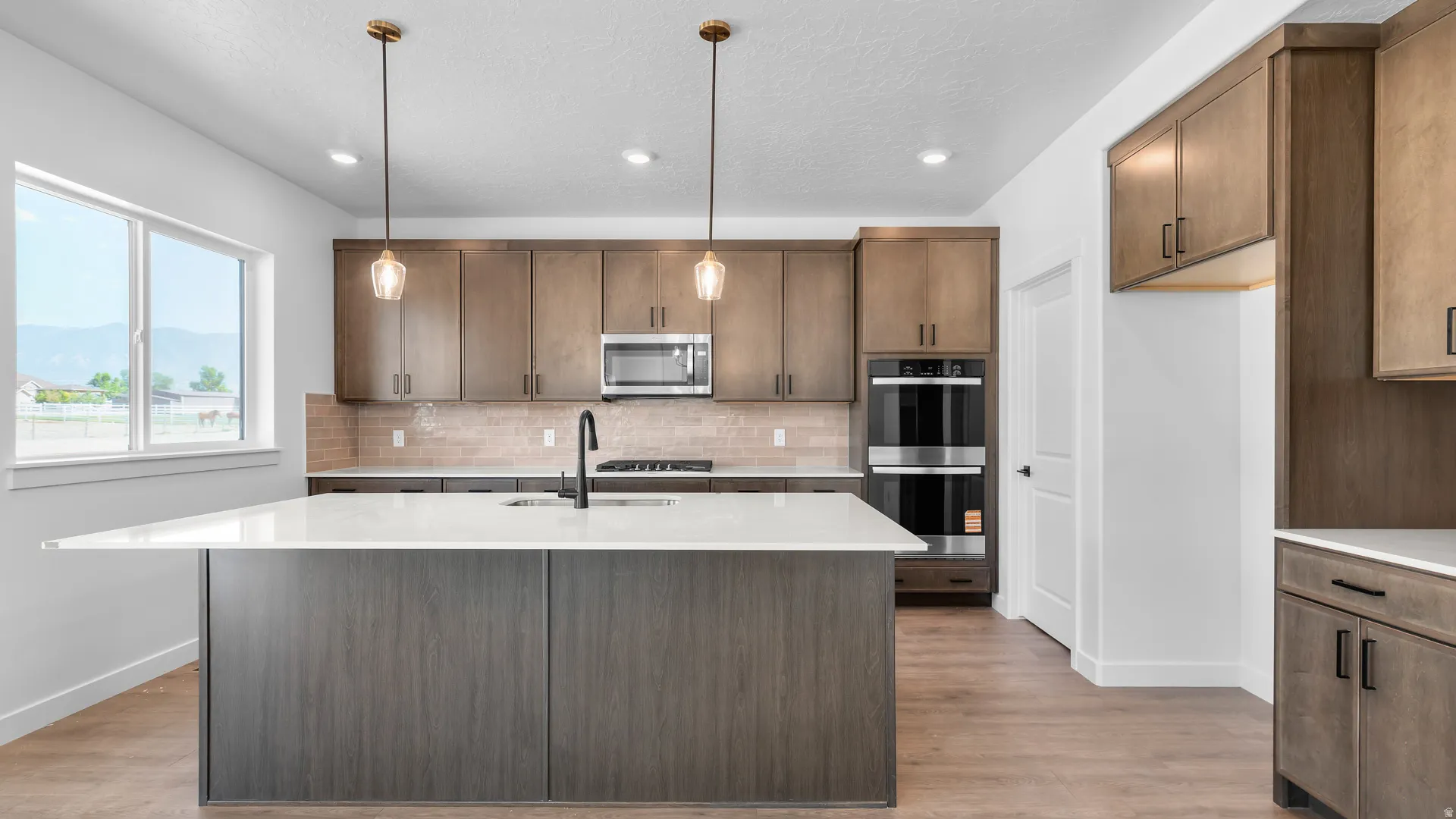 Modern kitchen featuring a large island with white countertop, wood-finish cabinetry, stainless steel appliances, and wood-finish flooring