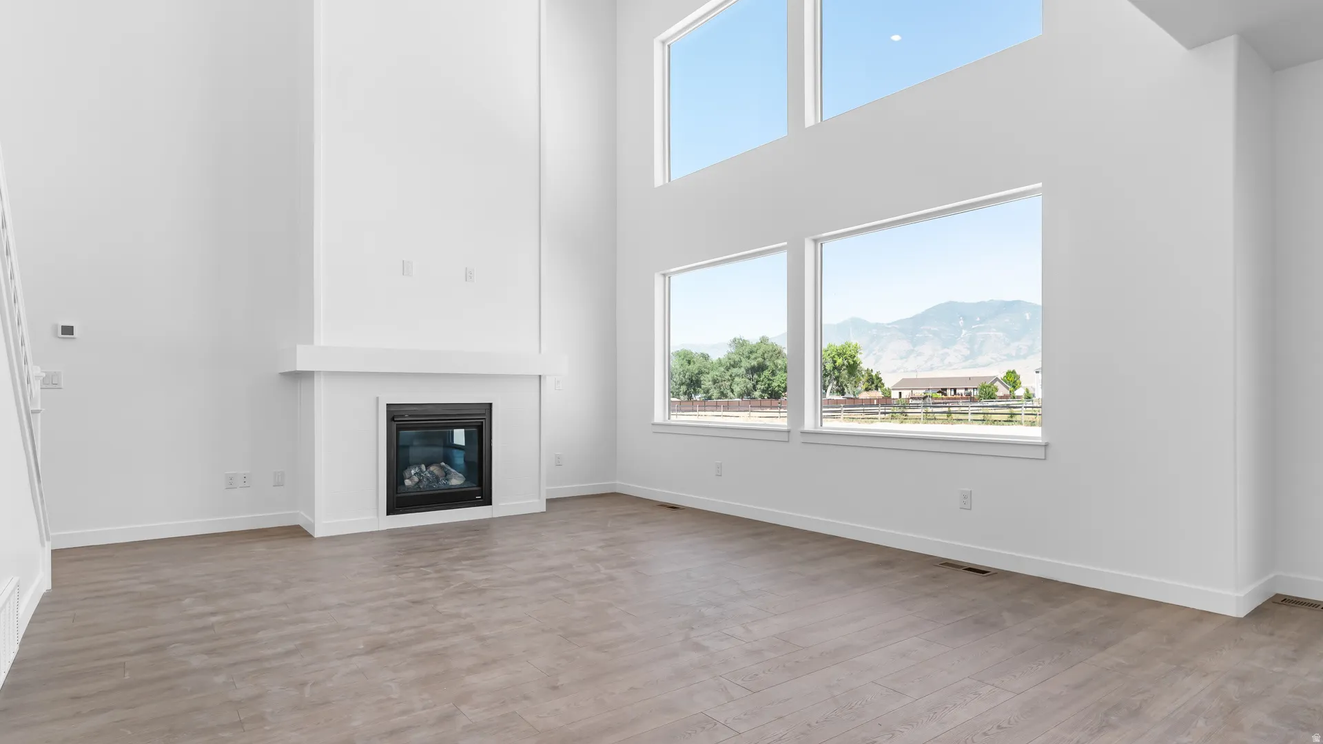 Soaring ceiling, contemporary fireplace with mantel, expansive windows, wood-finish flooring, and crisp white walls