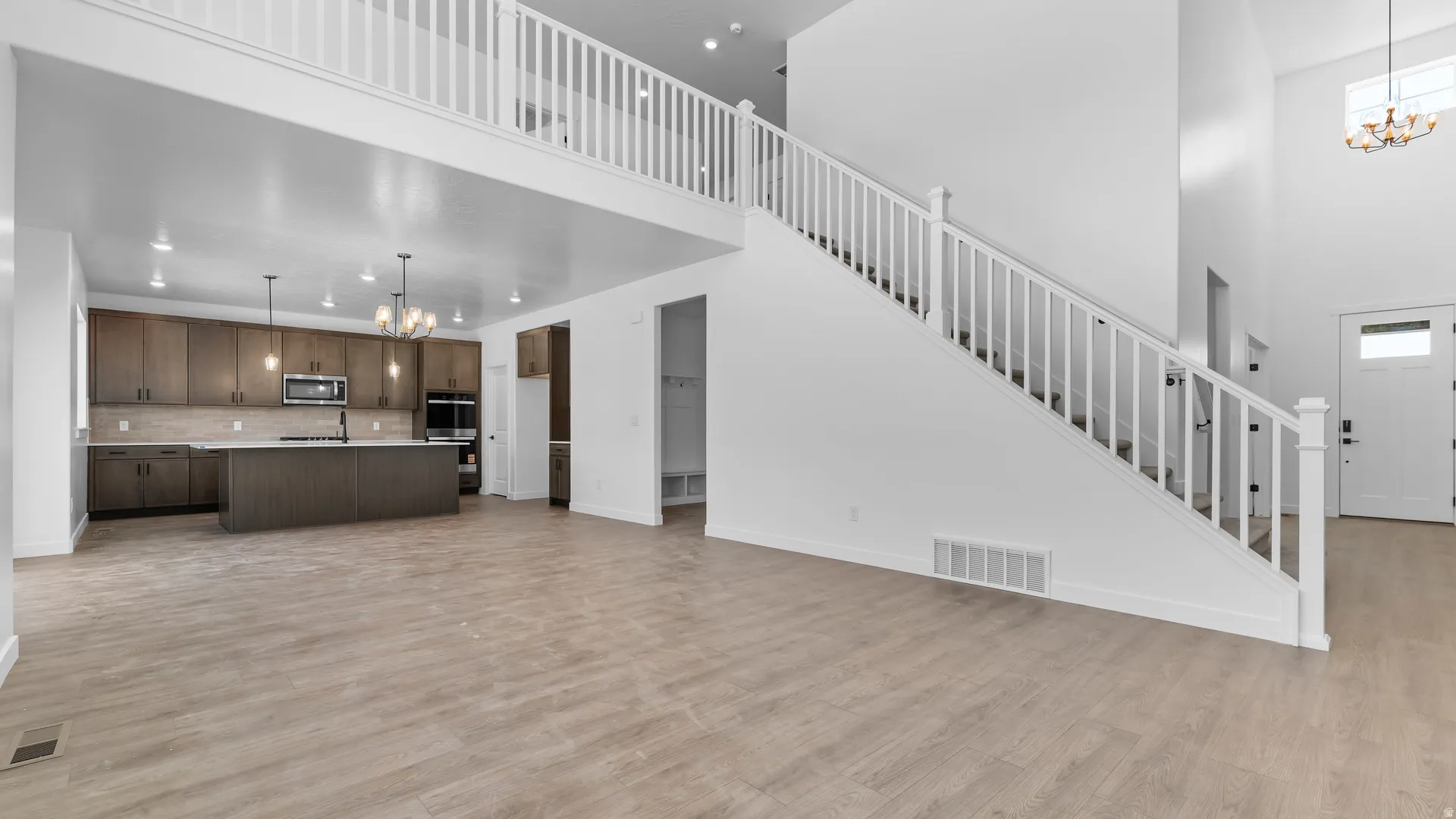 Open-concept living space with wood-finish flooring, a contemporary kitchen featuring an island with a sink, and a prominent staircase with a white balustrade