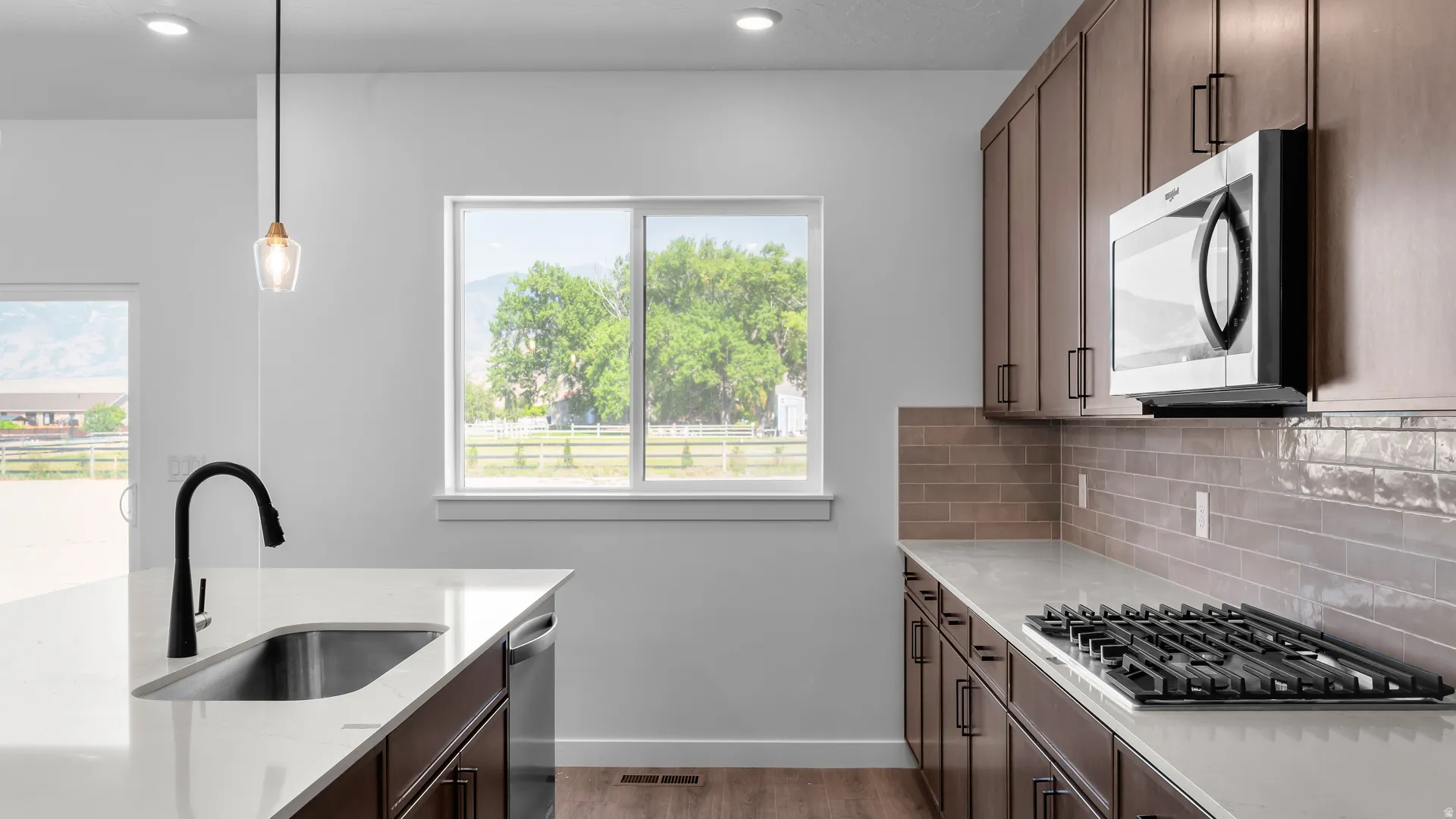 Kitchen featuring a stainless steel undermount sink with a gooseneck faucet, light-toned countertops, wood-finish cabinetry with linear hardware, a gas cooktop, and a built-in microwave