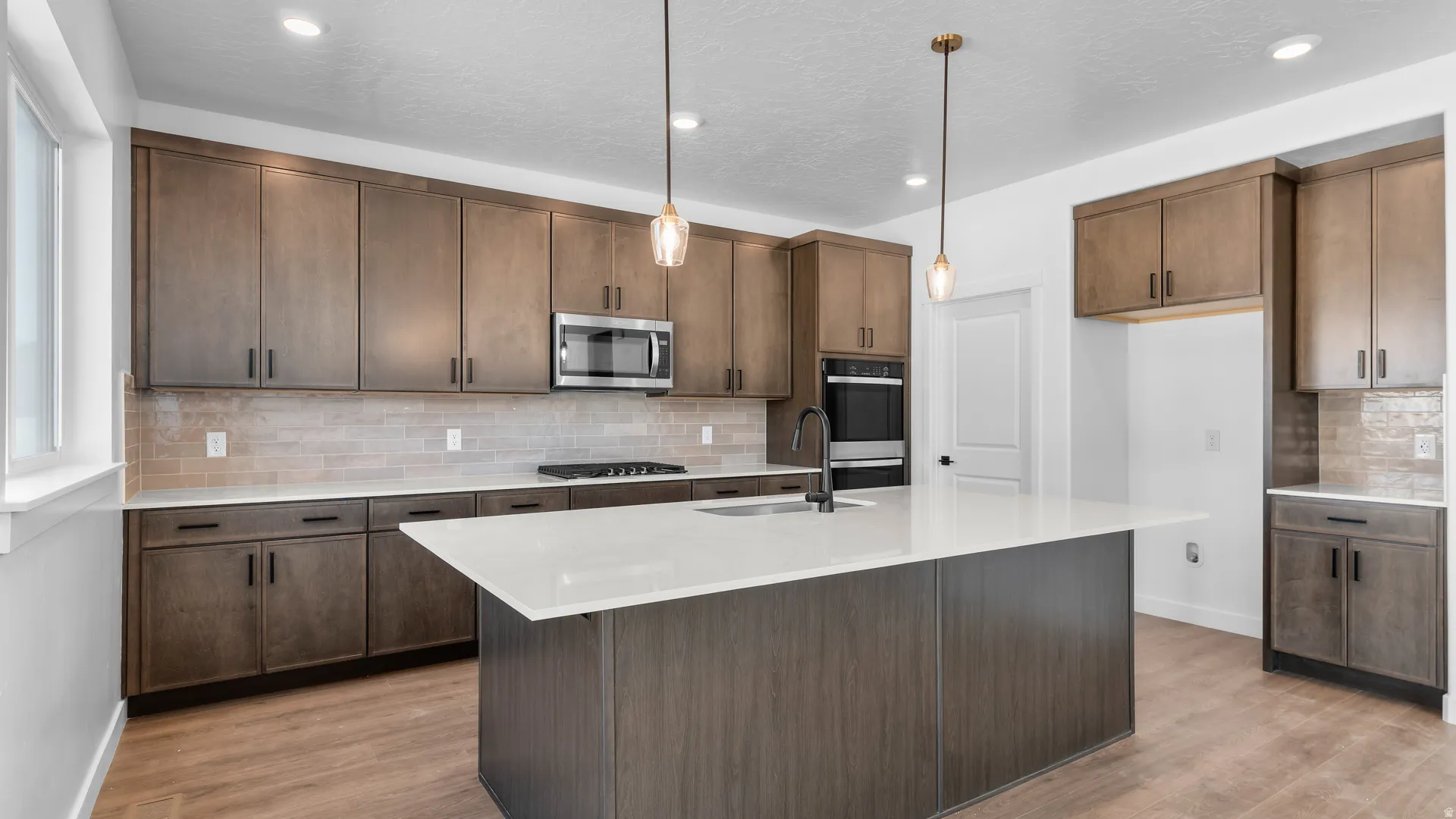 Kitchen featuring a large island with sink, extensive cabinetry, built-in oven, and a microwave