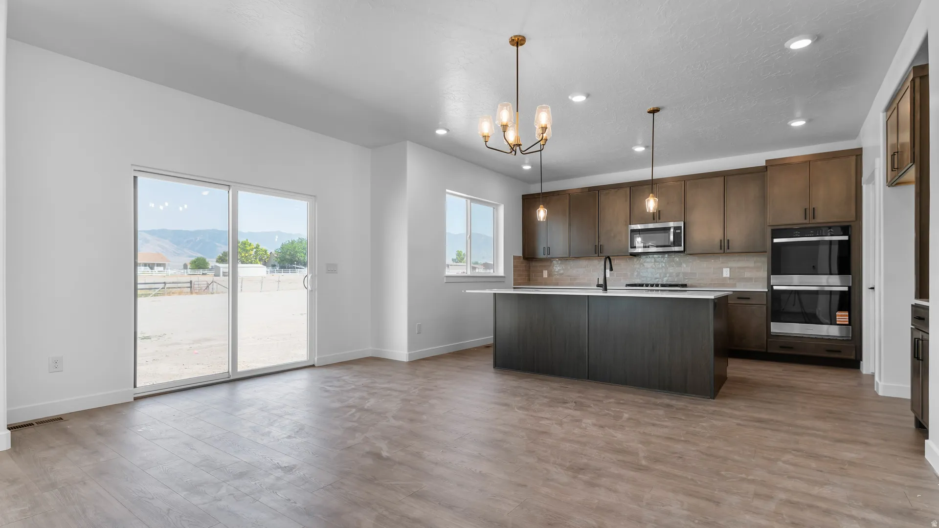 Open-concept kitchen and living area featuring wood-finish flooring, a kitchen island with a light-toned countertop, and dark wood cabinetry
