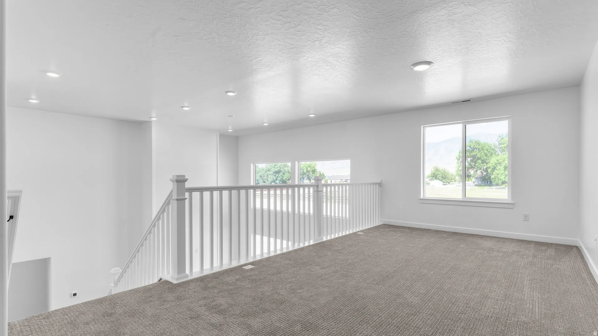 Carpeted loft area featuring a white railing, recessed ceiling lighting, and multiple windows