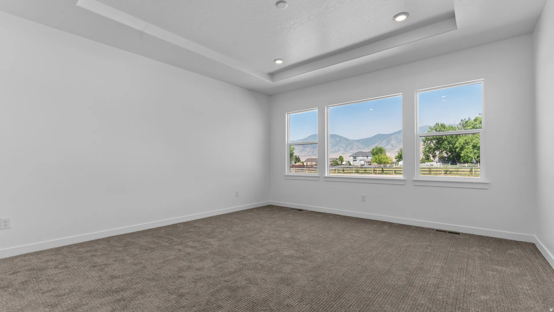 Recessed lighting, tray ceiling, wall-to-wall carpeting, and three expansive windows showcasing mountain scenery