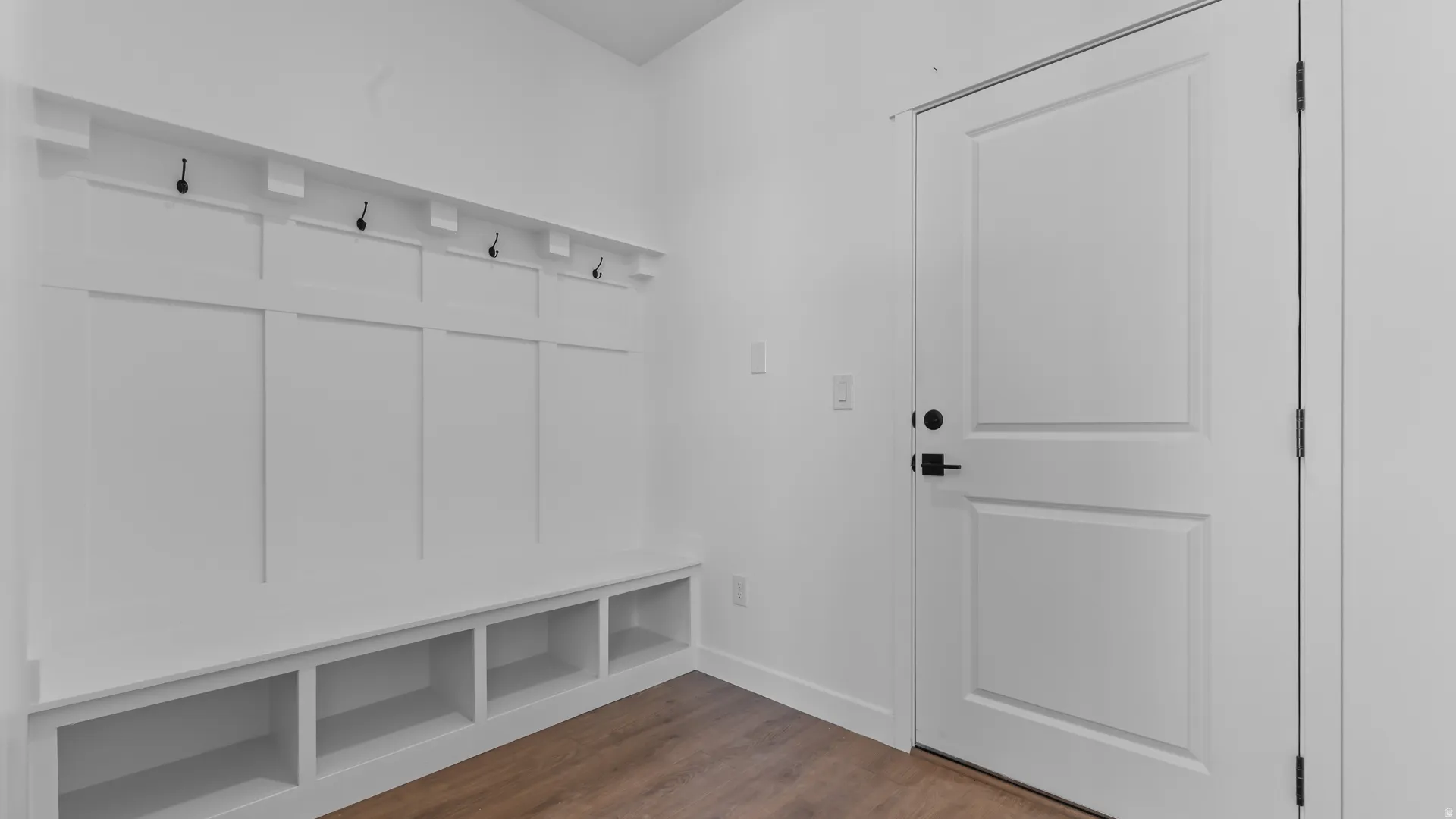 Built-in bench with cubby storage, wall-mounted coat hooks, wood-finish flooring, and a paneled interior door with matte black hardware