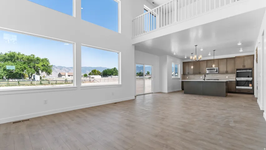 Two-story ceiling with a balcony, large windows, wood-finish flooring, sliding glass doors, and a kitchen with an island