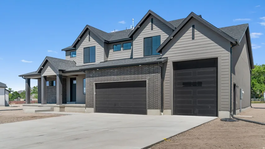 Modern exterior featuring black brick accents, gray siding, a multiple-car garage, and a covered entry