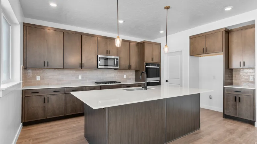 Kitchen featuring a large island with sink, extensive cabinetry, built-in oven, and a microwave