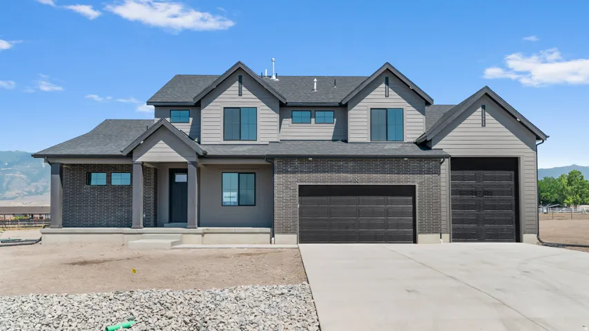 Contemporary two-story residence with a multi-gabled roofline, dark brick accents, light gray siding, a covered entry porch, and an attached three-car garage