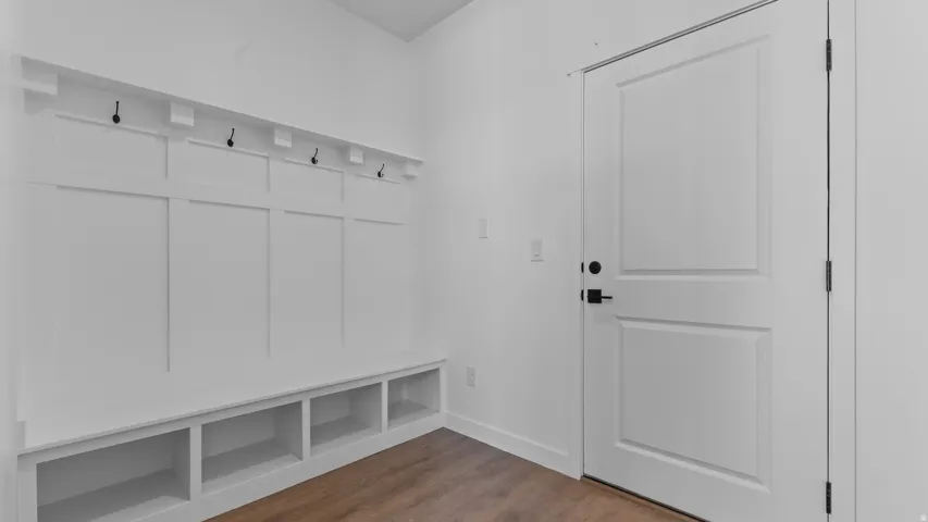 Built-in bench with cubby storage, wall-mounted coat hooks, wood-finish flooring, and a paneled interior door with matte black hardware