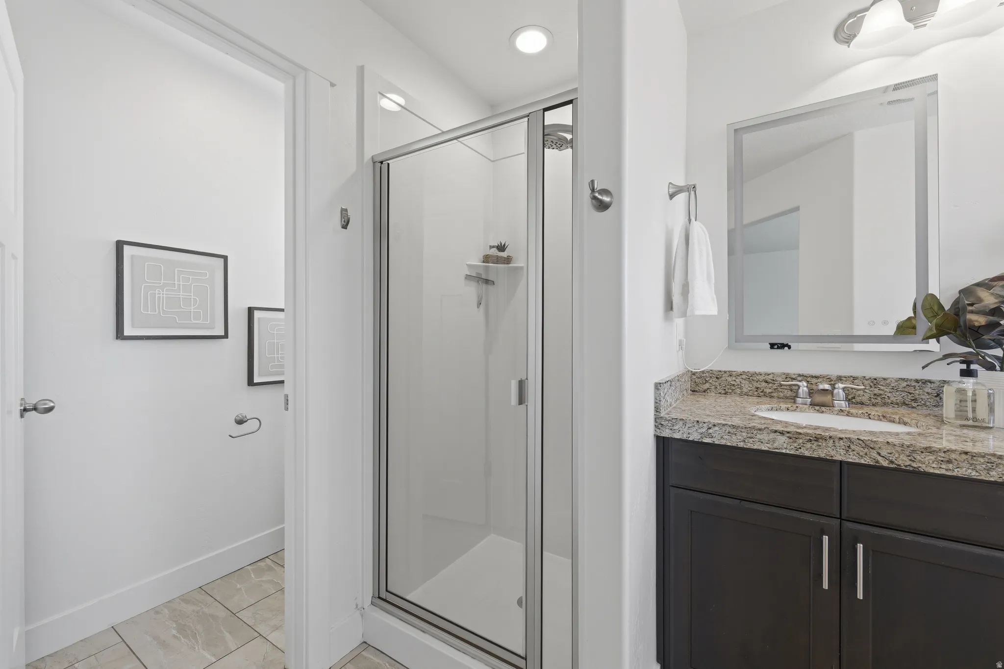 Shower enclosure with clear glass door, dark wood-finish vanity with a light-toned countertop, integrated sink, and a framed mirror