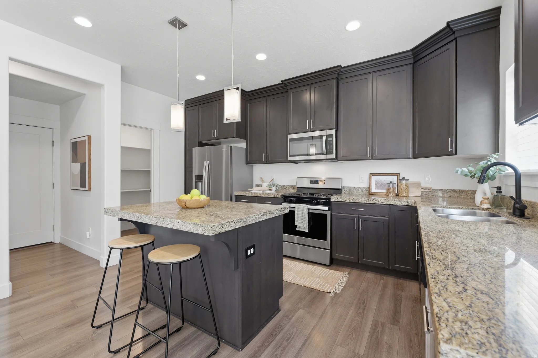 Kitchen featuring dark wood-finish cabinetry, granite countertops, stainless steel appliances, a center island with pendant lighting, and wood-finish flooring