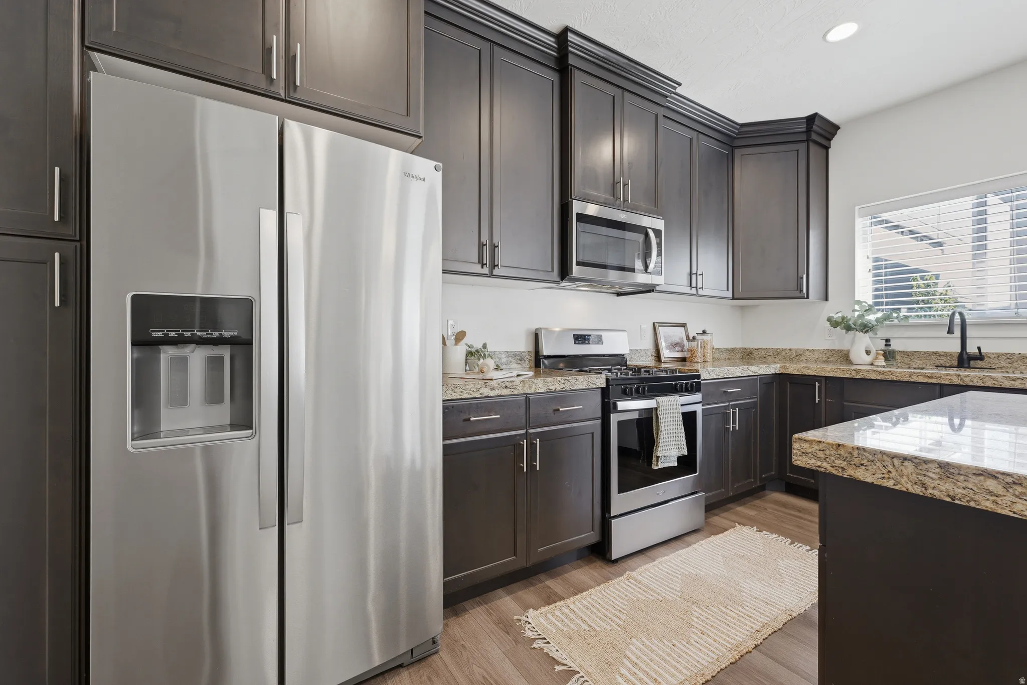 Kitchen featuring stainless steel appliances, dark wood-finish cabinetry, light-toned countertops, wood-finish flooring, and a built-in microwave