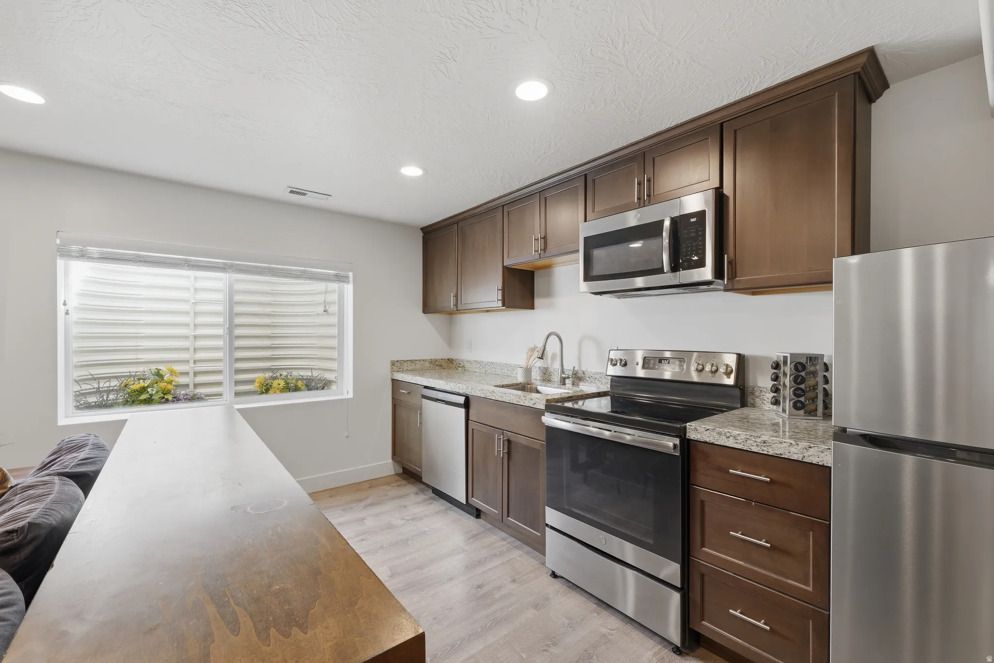 Kitchen featuring stainless steel appliances, wood-finish cabinetry, stone countertops, and wood-finish flooring