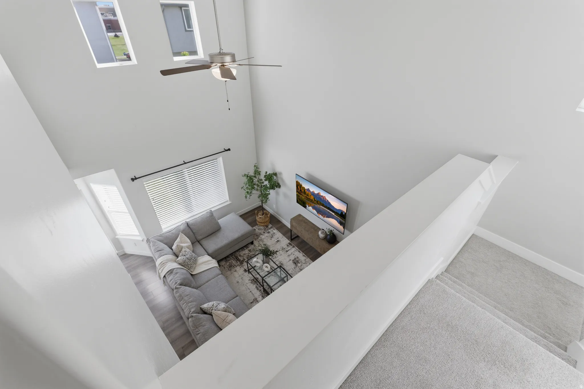 Two-story living area with high ceilings, wood-finish flooring, and a ceiling fan