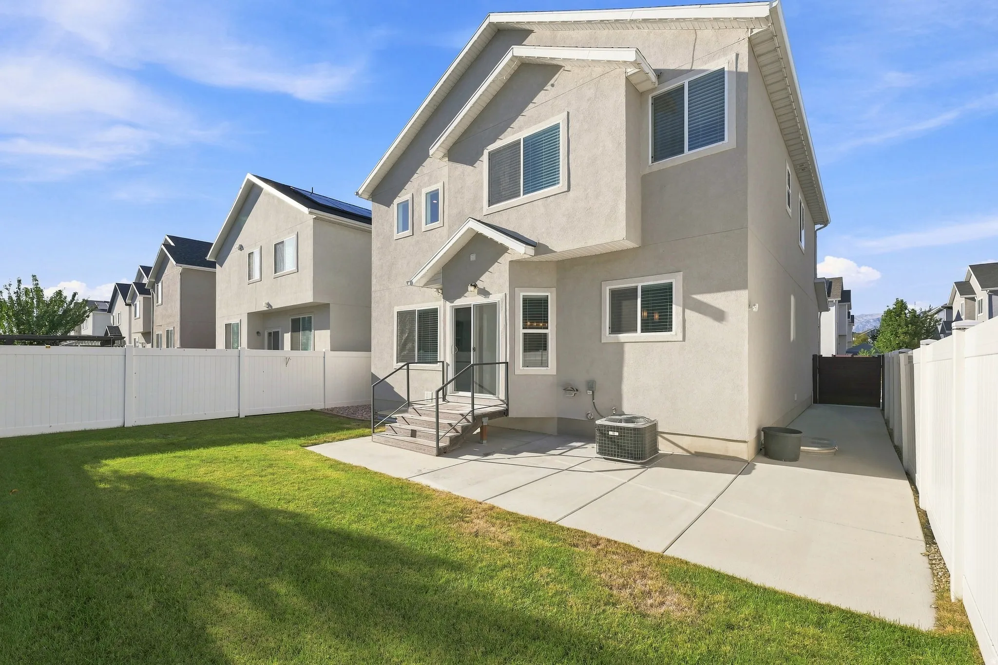 Expansive lawn area, concrete patio, white privacy fencing, exterior stucco finish, and a rear deck with steps