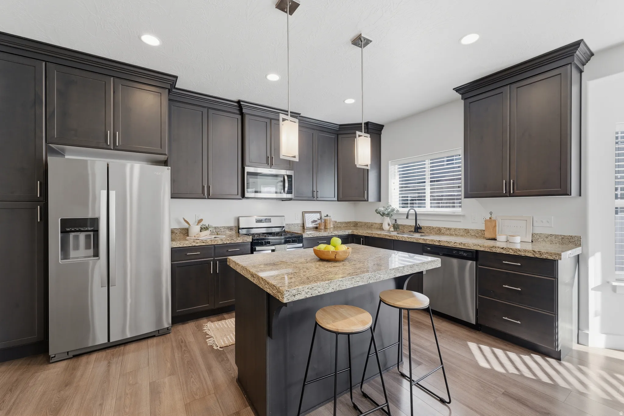 Dark wood cabinetry, stainless steel appliances, wood-finish flooring, recessed lighting, and a kitchen island with stone countertop