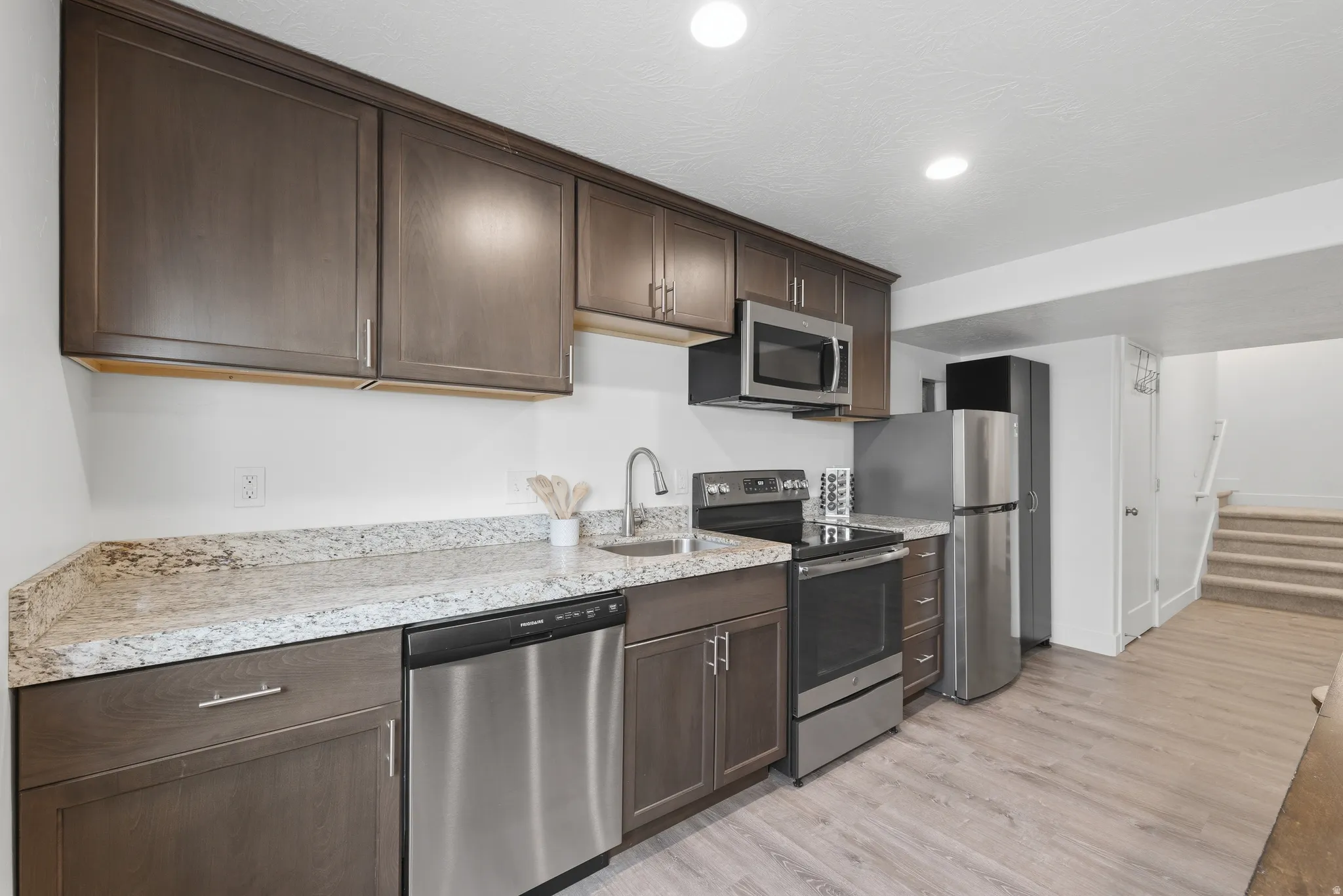 Dark wood-finish cabinetry with stainless steel hardware, light-toned speckled countertops, and stainless steel appliances
