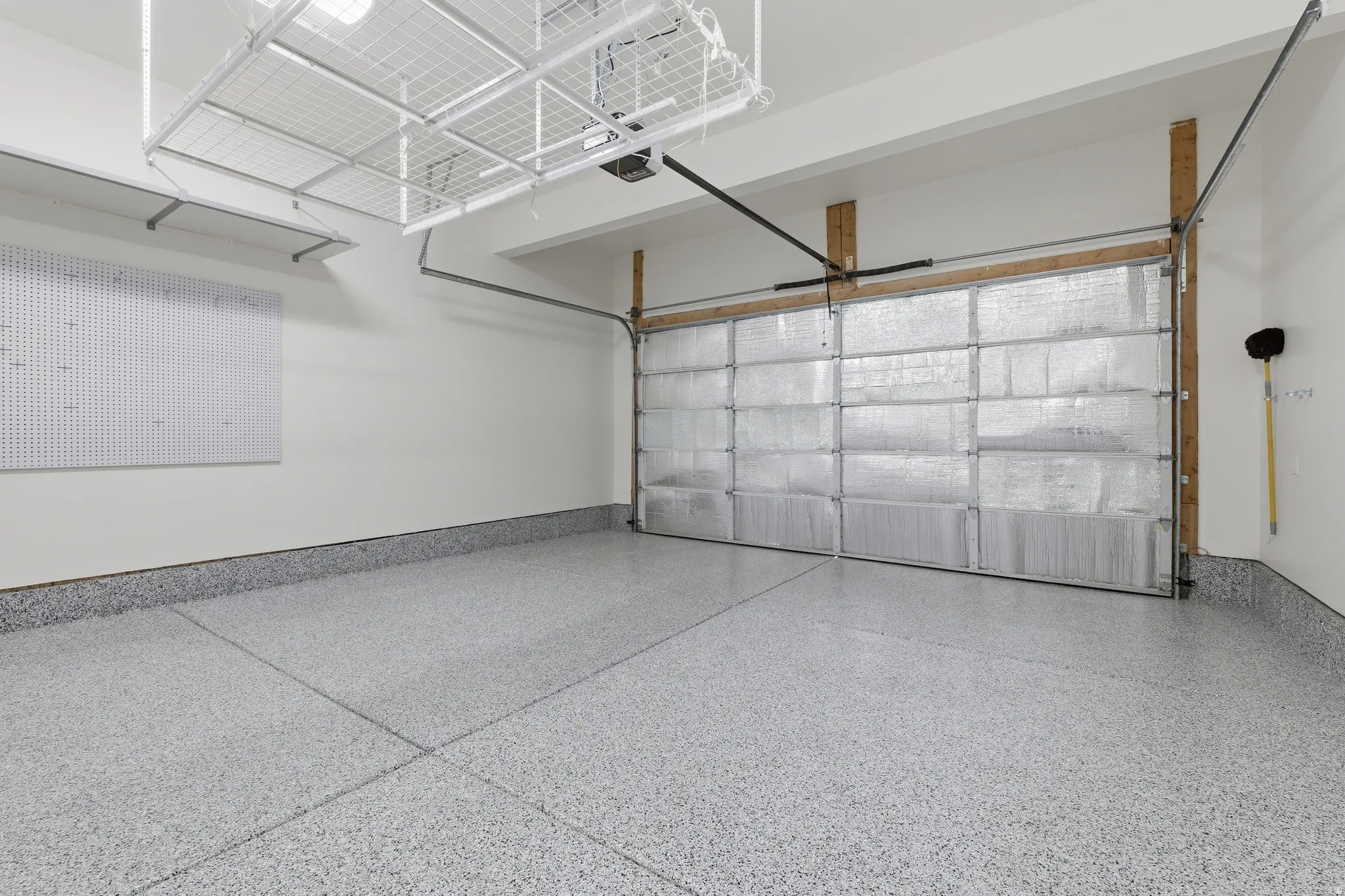Epoxy-coated flooring, insulated garage door, integrated wall organization system, overhead storage racks, and white wall finishes