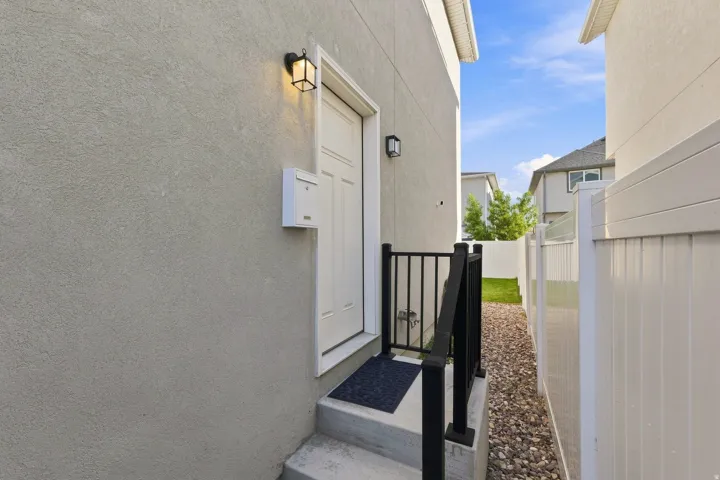 Stucco exterior, white paneled entry door, black metal railing, gravel pathway, and white privacy fence
